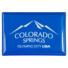 Load image into Gallery viewer, Blue rectangular, shiny magnet with white Colorado Springs: Olympic City USA logo printed onto it
