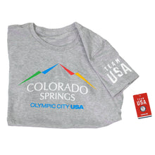 Load image into Gallery viewer, Horizontally folded in half gray short sleeved t-shirt with full color version of the city of Colorado Springs: Olympic City USA logo. Team USA printed in white on the right sleeve.