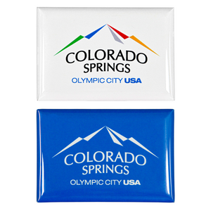 2 rectangular, shiny magnets. Both have printed artwork. One includes a full colored Colorado Springs: Olympic City USA logo on a white background, and the other is the same logo white on top of a blue background.  
