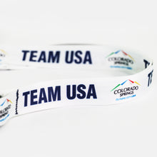 Load image into Gallery viewer, Up close view of the with official City of Colorado Springs: Olympic City USA and Team USA logos and wordmarks decorating a white lanyard
