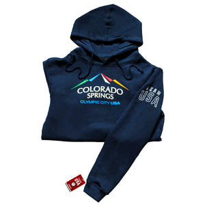 Folded horizontally in half navy pullover hoodie with hoodie strings attached to hood. Color version of the city of Colorado Springs: Olympic City USA logo printed in center. Team USA printed in white omn the upper right sleeve. Team USA tag attached to bottom of same sleeve.
