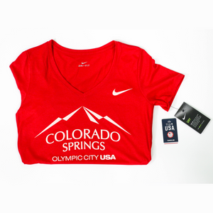 Folded in half horizontally red short sleeve v-neck t-shirt with white version of the city of Colorado Springs: Olympic City USA logo printed on front. White Nike logo under right shoulder. Team USA and Nike tags attached to right sleeve.